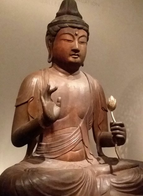 Photo of sculpture of seated Buddha holding golden flower